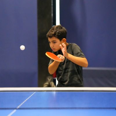 A young boy returning a serve while playing table tennis at ISD Table Tennis Academy